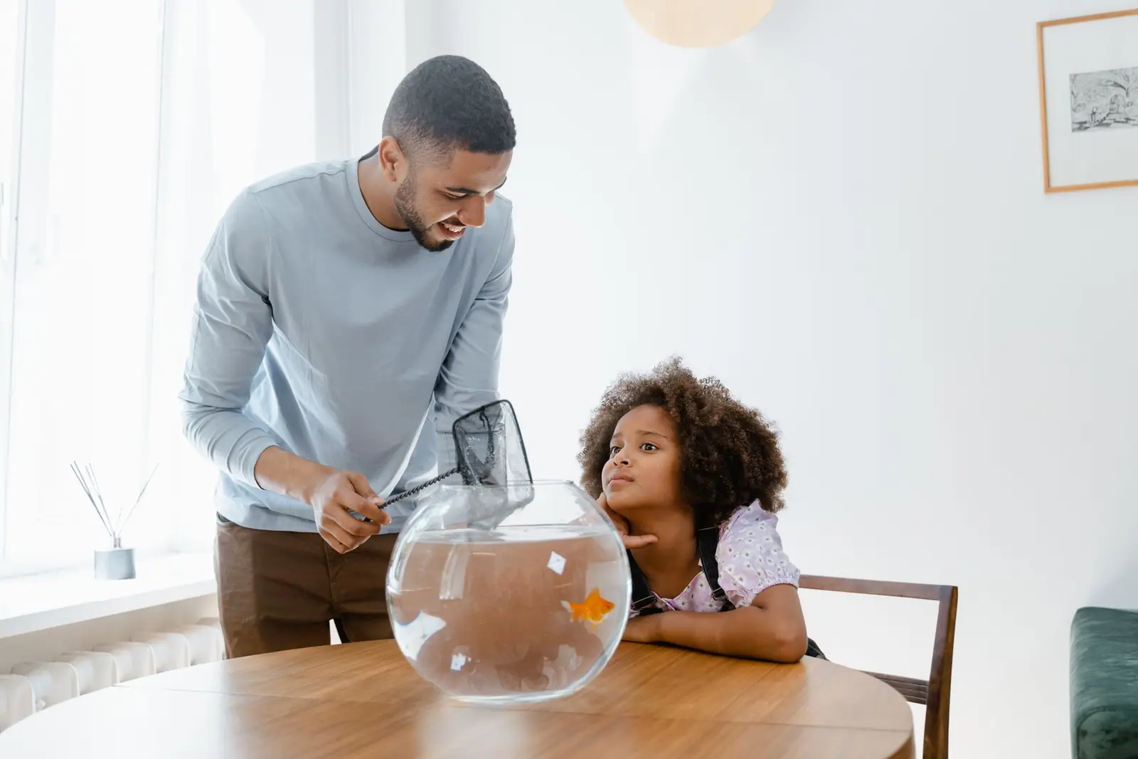 A man holding a small fish net over a bowl while a child watches
