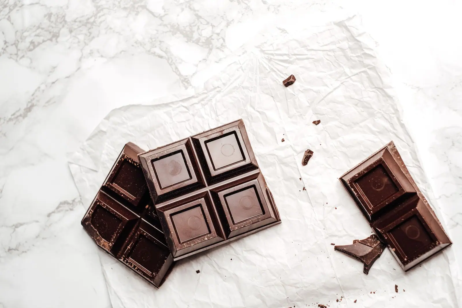Squares of dark chocolate broken apart on white paper